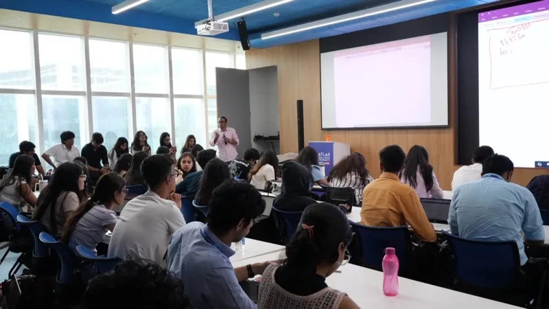 Presenter speaking to a large classroom with a projector screen